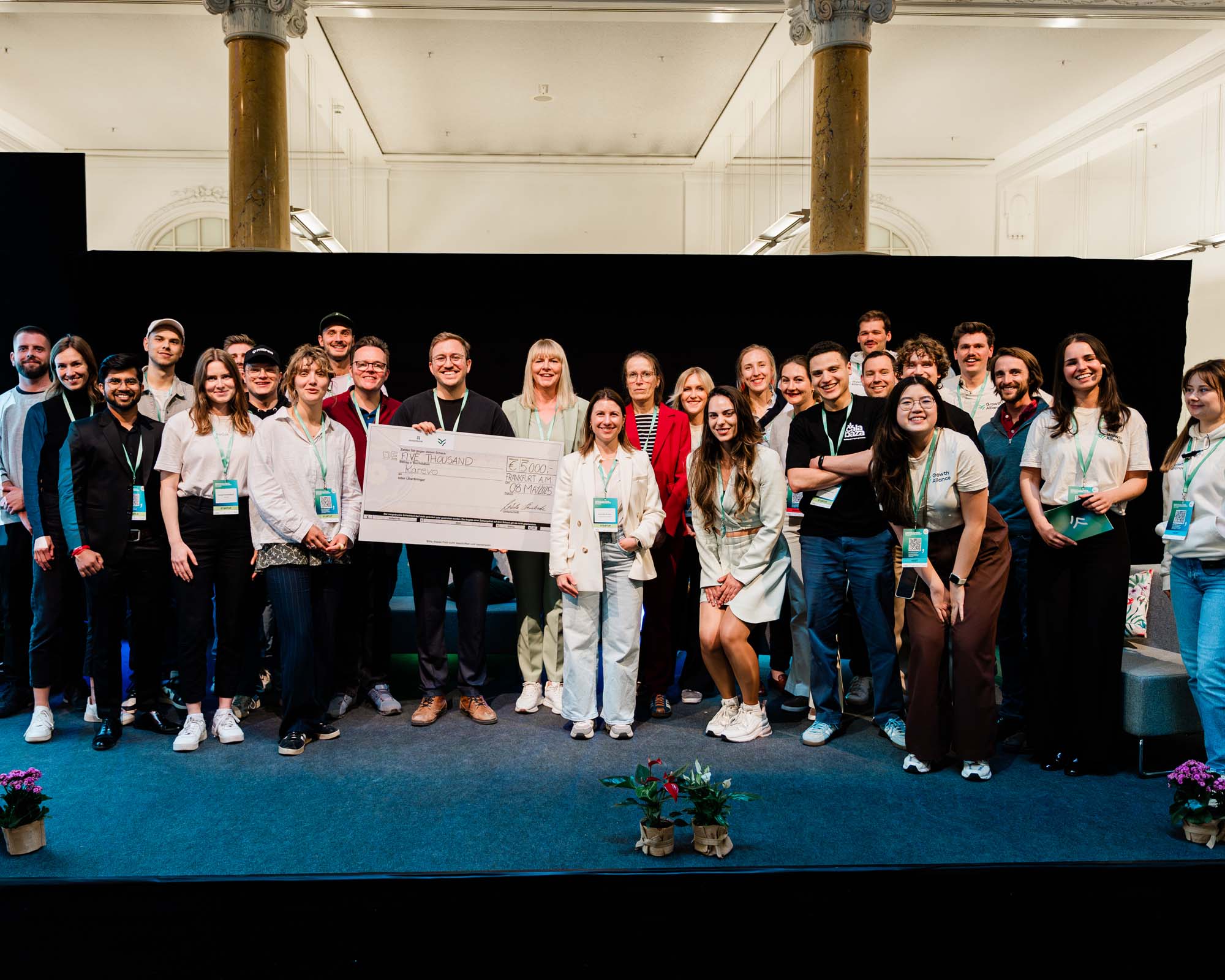 Gruppe von Teilnehmenden der Veranstaltung GANS in 2025 steht auf einer Bühne, einige halten einen großen symbolischen Scheck, alle lächeln in die Kamera.